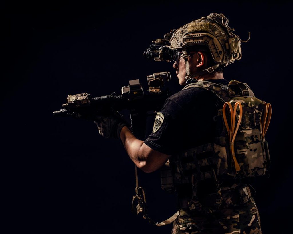 Portrait of a soldier in tactical gear holding a rifle in a studio setting.